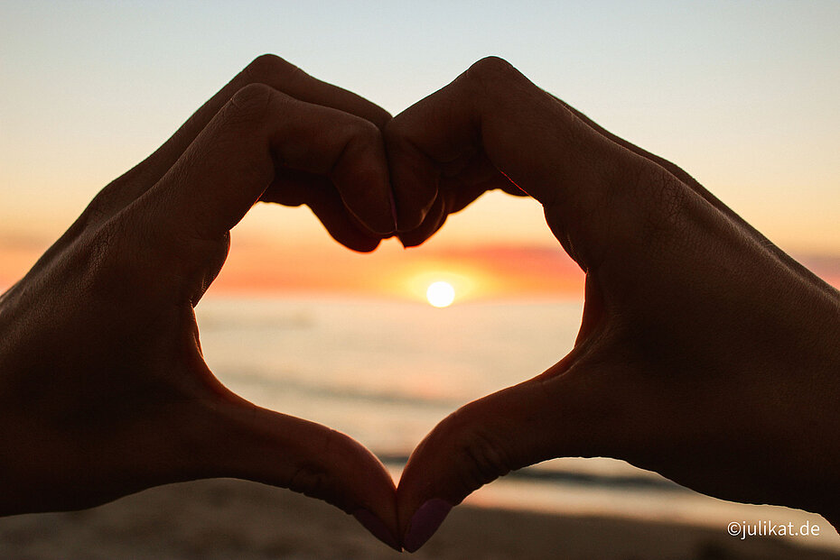 Hand in Form eines Herzens mit Sonnenuntergang im Hintergrund